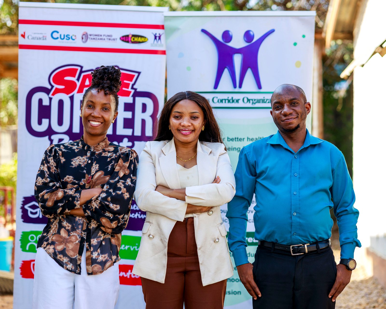 Three Teens Corridor team members smile in front of the Safe Corner and Teens Corridor banners