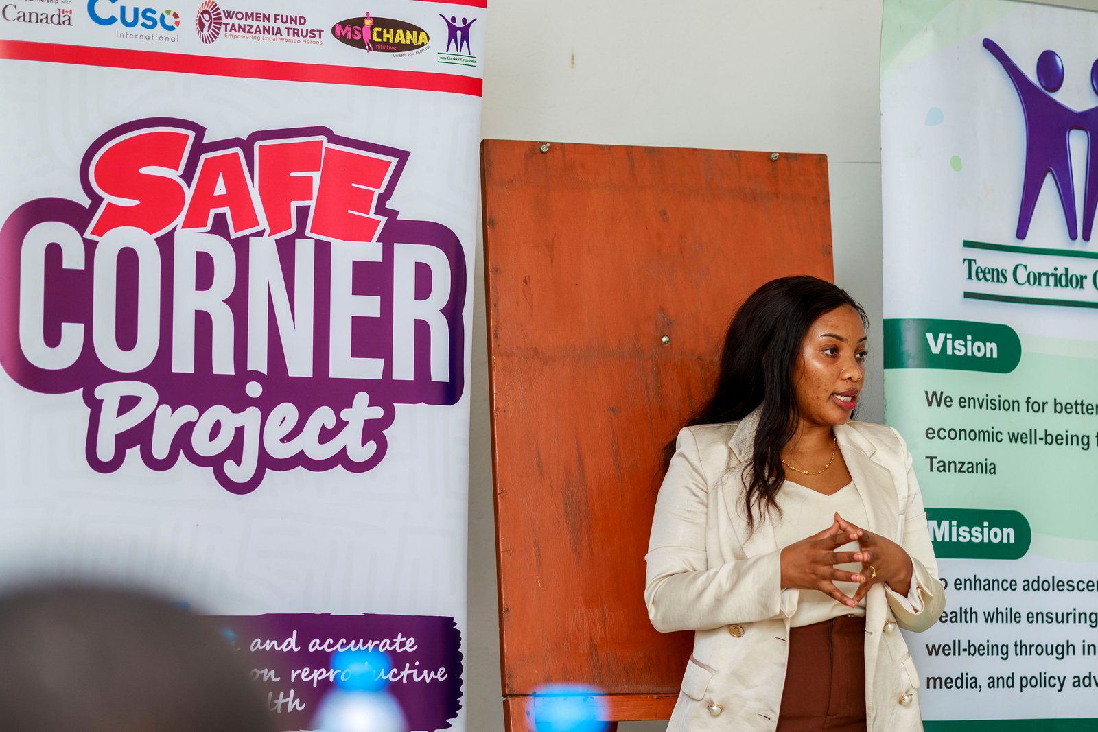 A Safe Corner Project facilitator speaks beside banners on youth-friendly reproductive health information
